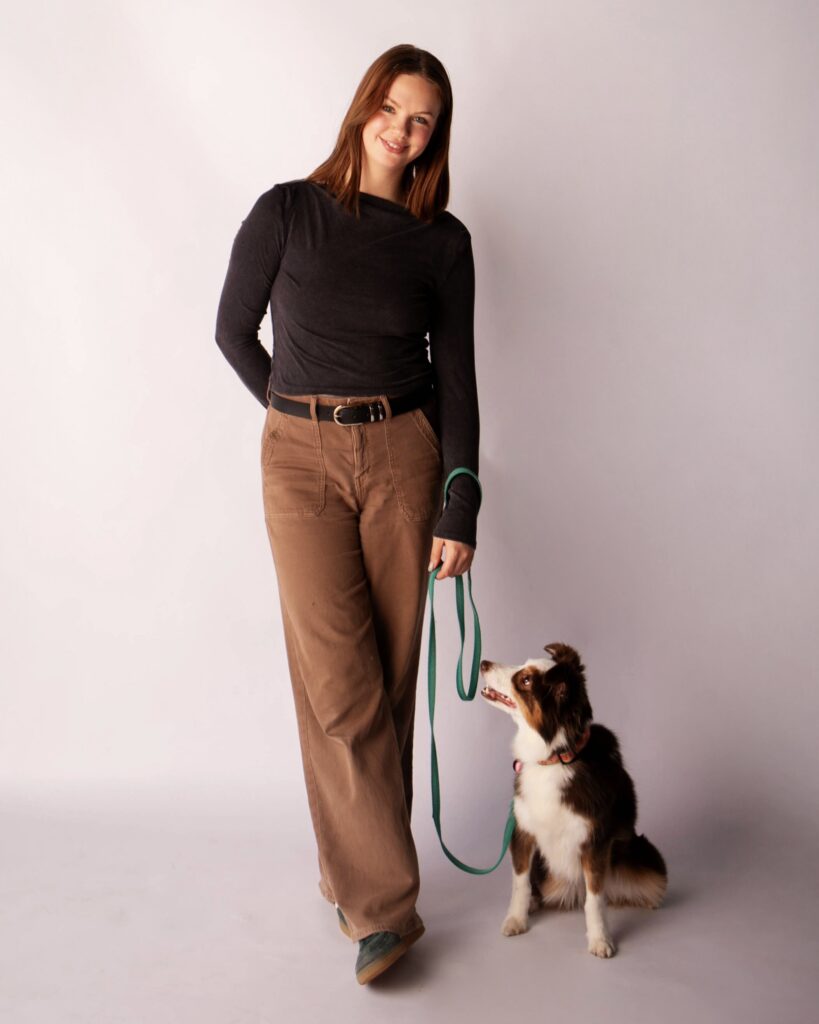 Woman standing with a medium sized dog on leash that is sitting by her side